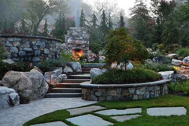 Terraced stone garden with outdoor fireplace at dusk
